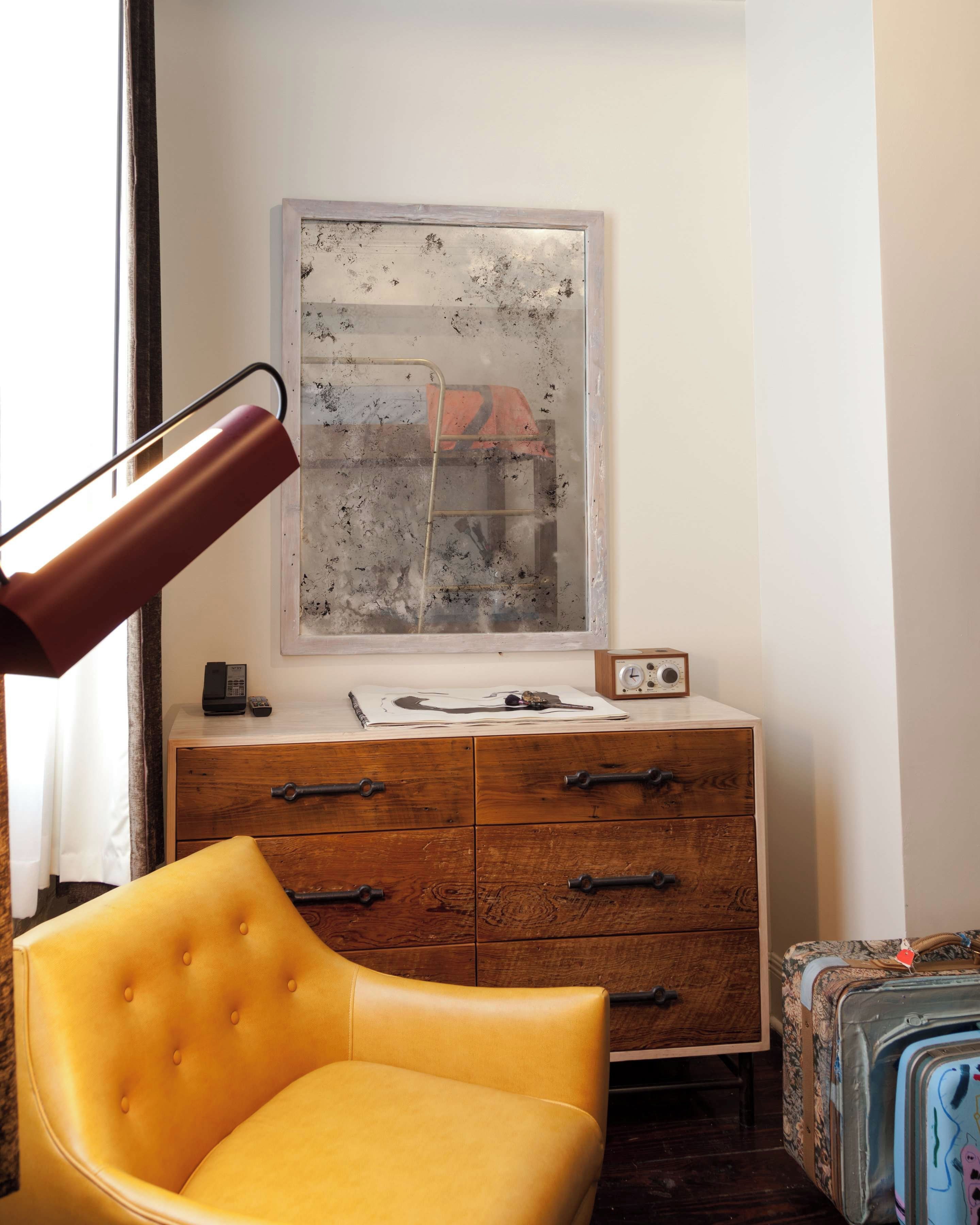 A room with a yellow chair, wooden dresser, and a large window with a view.
