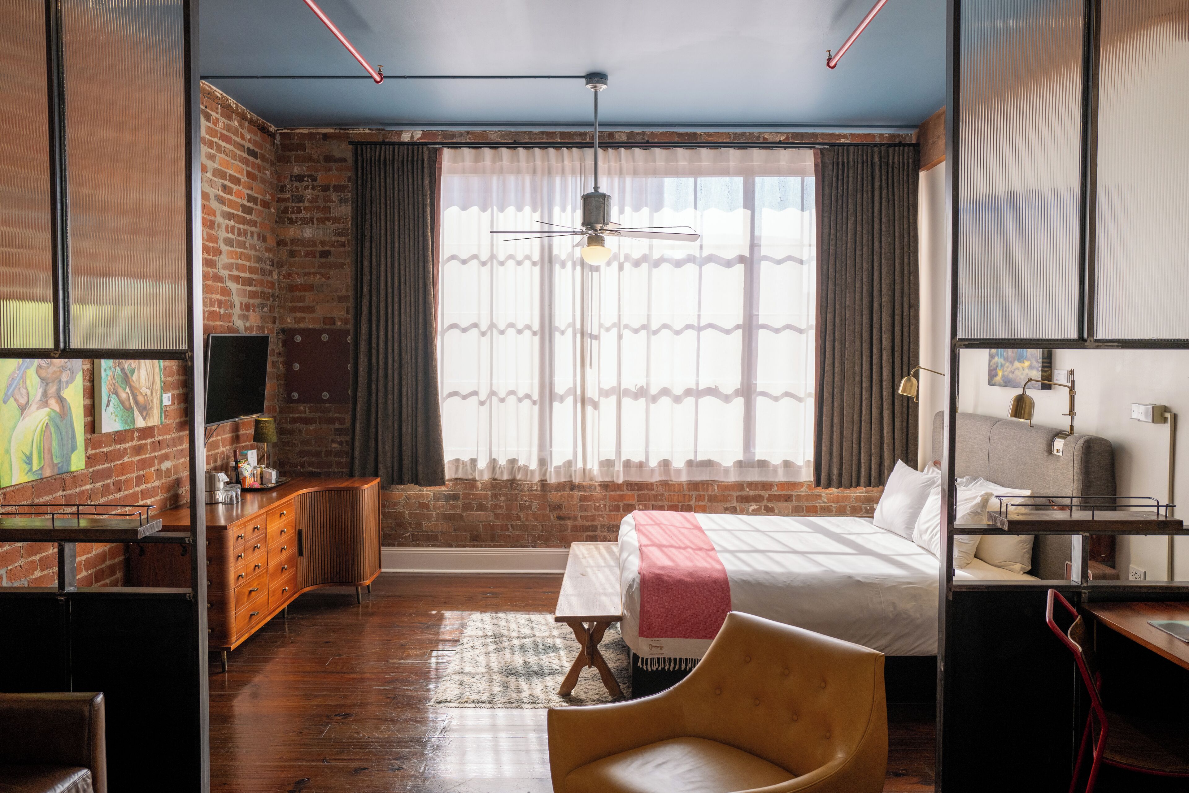 A hotel room with a bed, a desk, a chair, a TV, a wardrobe, and a large window with curtains.