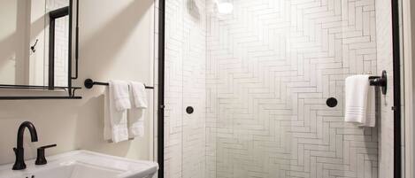 A bathroom with a white sink, toilet, and a shower with a herringbone tile pattern.
