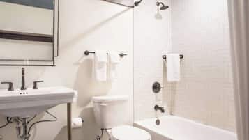 Ein Badezimmer mit Waschbecken, Toilette und Badewanne. Handtücher hängen an der Wand und eine Duschbrause ist vorhanden.