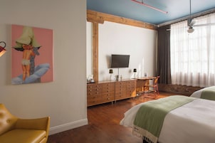 Habitación de hotel con un aparador de madera, televisor, escritorio, dos camas, una silla y un cuadro en la pared.