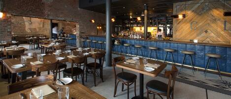 A restaurant with multiple tables and stools, a bar area, and a brick wall.