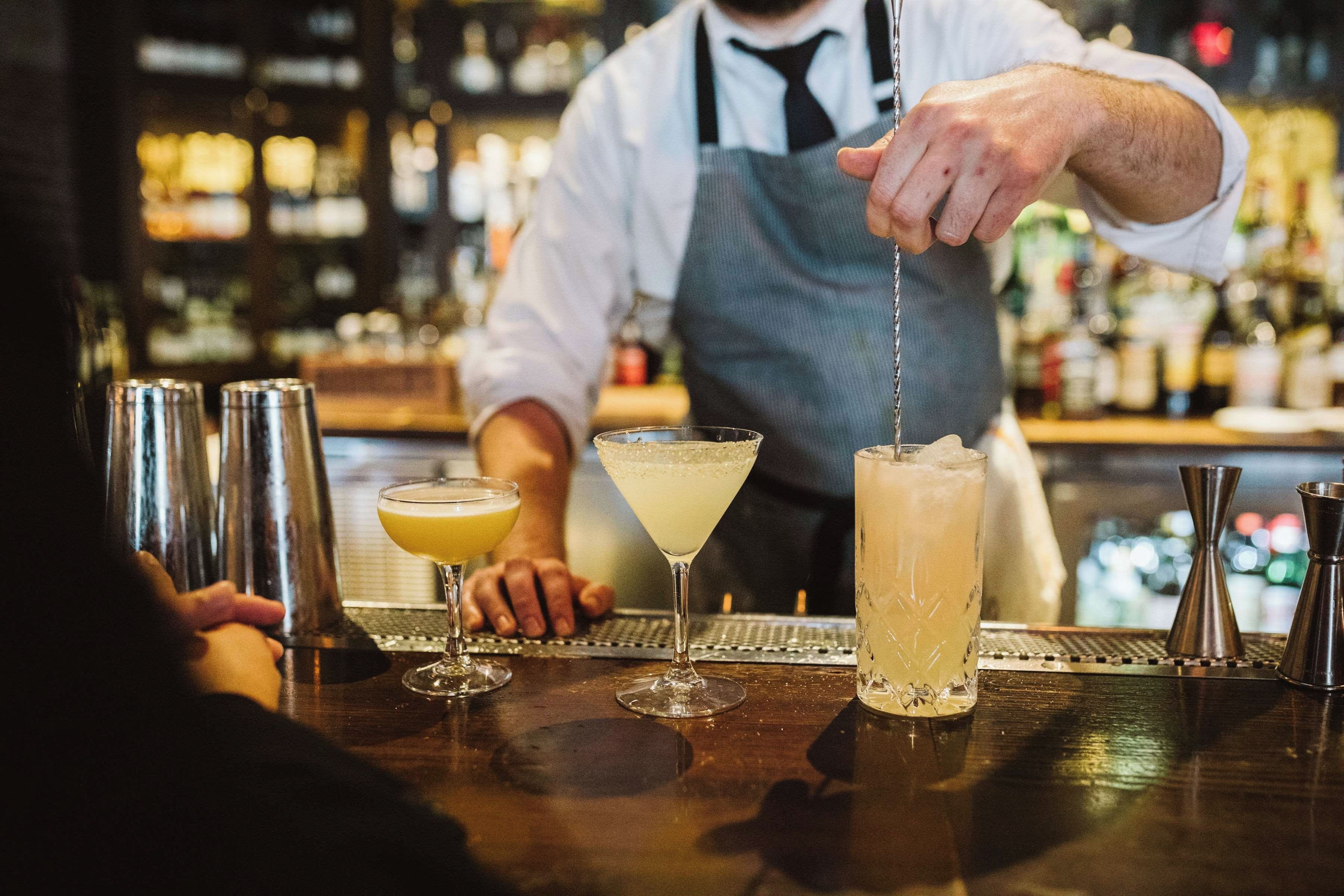 A bartender preparing drinks at a bar with a variety of cocktail glasses and bottles.