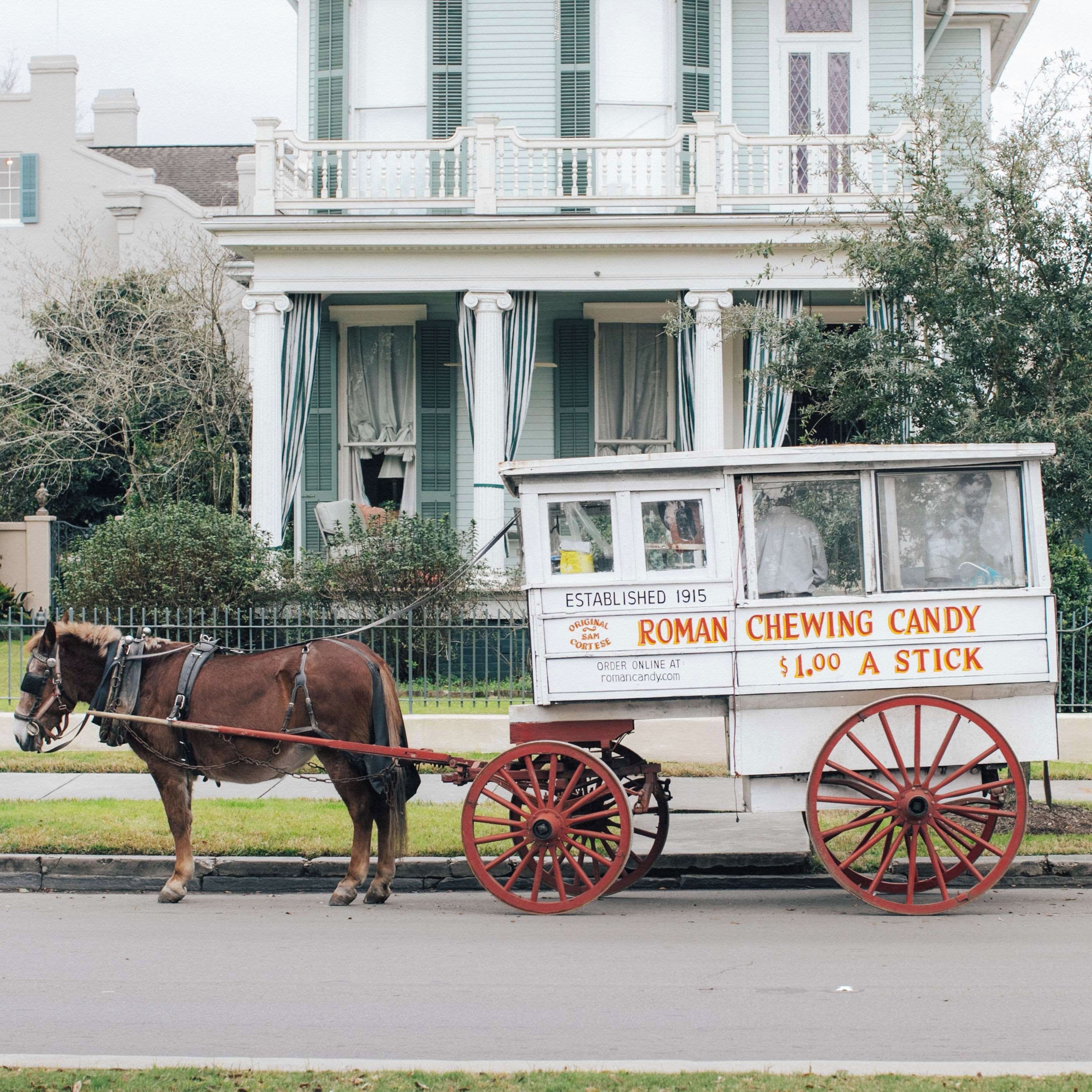A horse-drawn carriage with a sign advertising chewing candy, parked in front of a building with green shutters and a balcony.