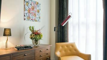 Una habitación de hotel con un aparador de madera, un florero con flores, un libro titulado 'Making New Orleans', una lámpara, una silla y un cuadro en la pared.