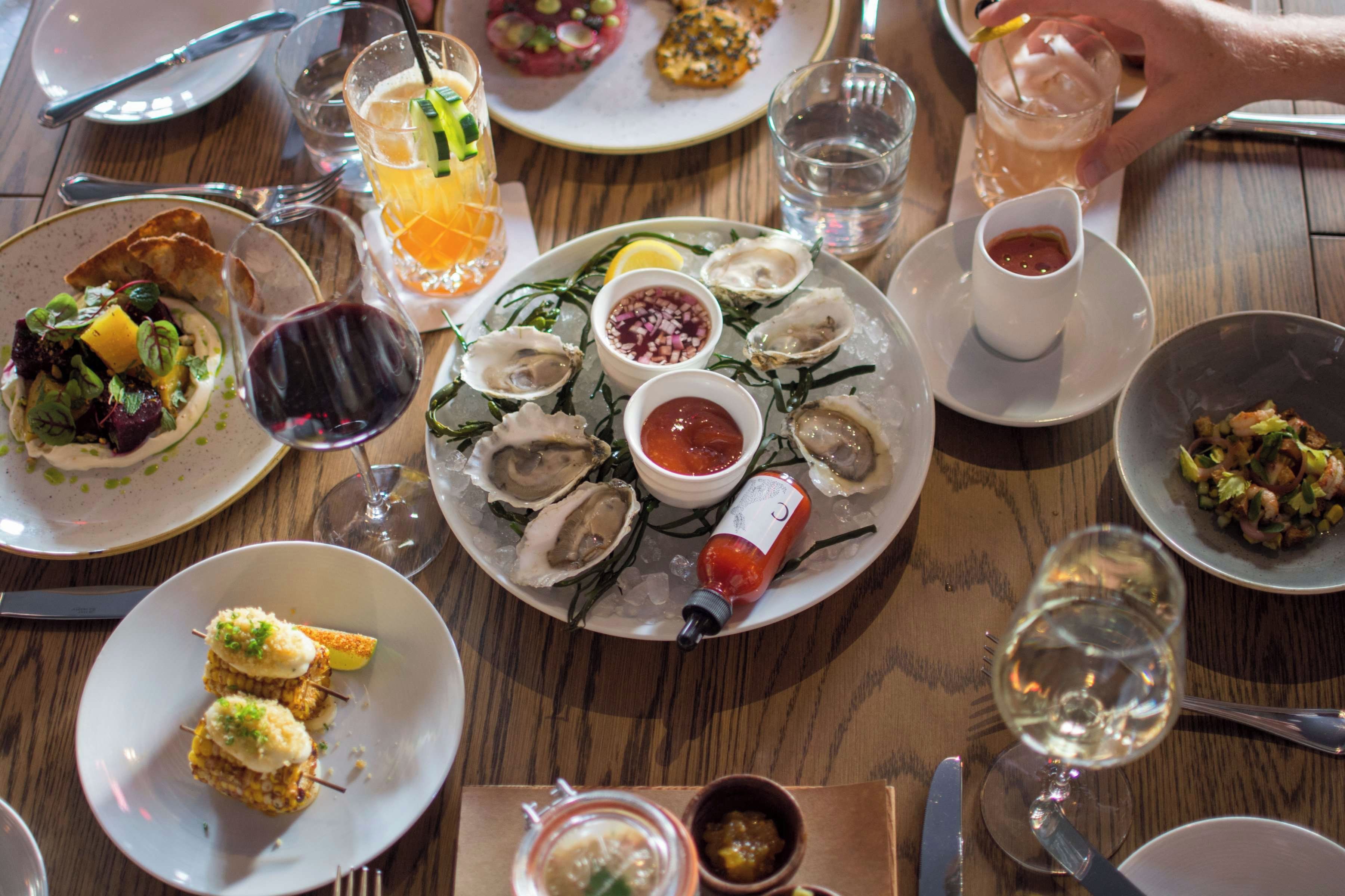 A dining table with various dishes, including oysters on ice, a salad, and a glass of orange juice.