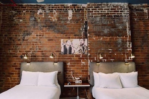 A room with two beds, a brick wall, and a picture above the beds.