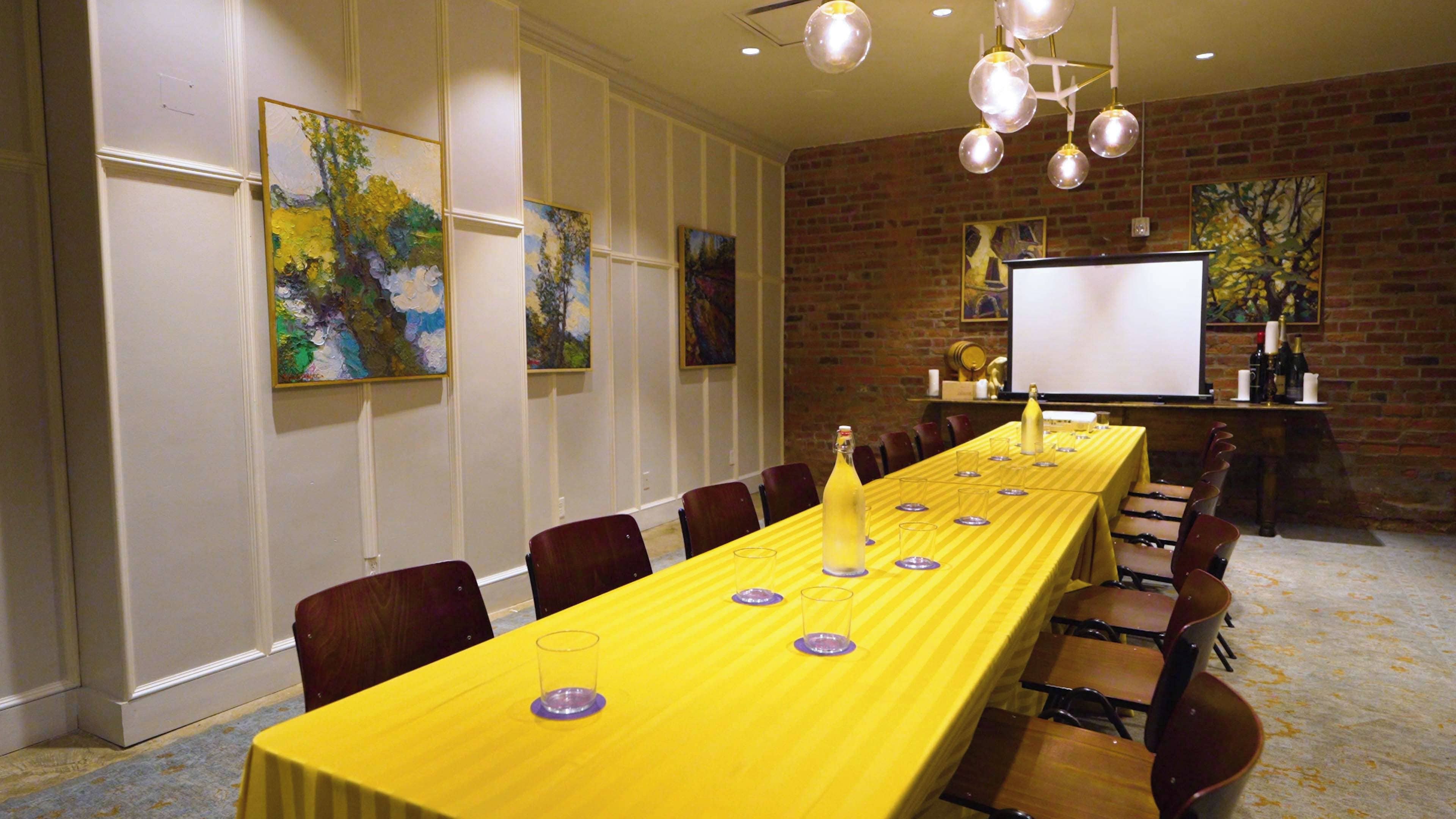 A conference room with a long table, chairs, a projector screen, and artwork on the walls.