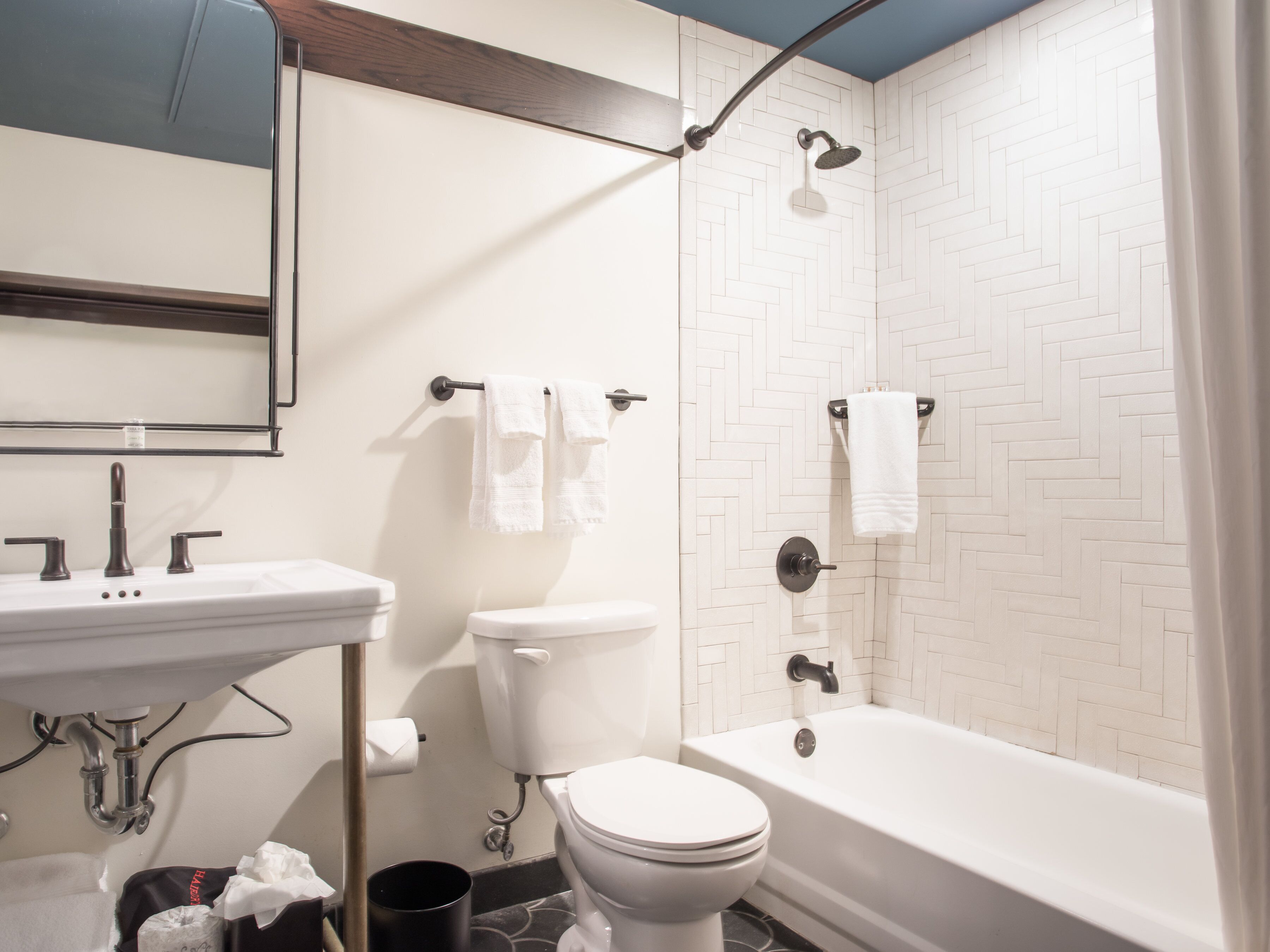 Une salle de bain moderne avec un lavabo, des toilettes et une baignoire blancs. Des serviettes sont accrochées au mur et une pomme de douche se trouve au-dessus de la baignoire.