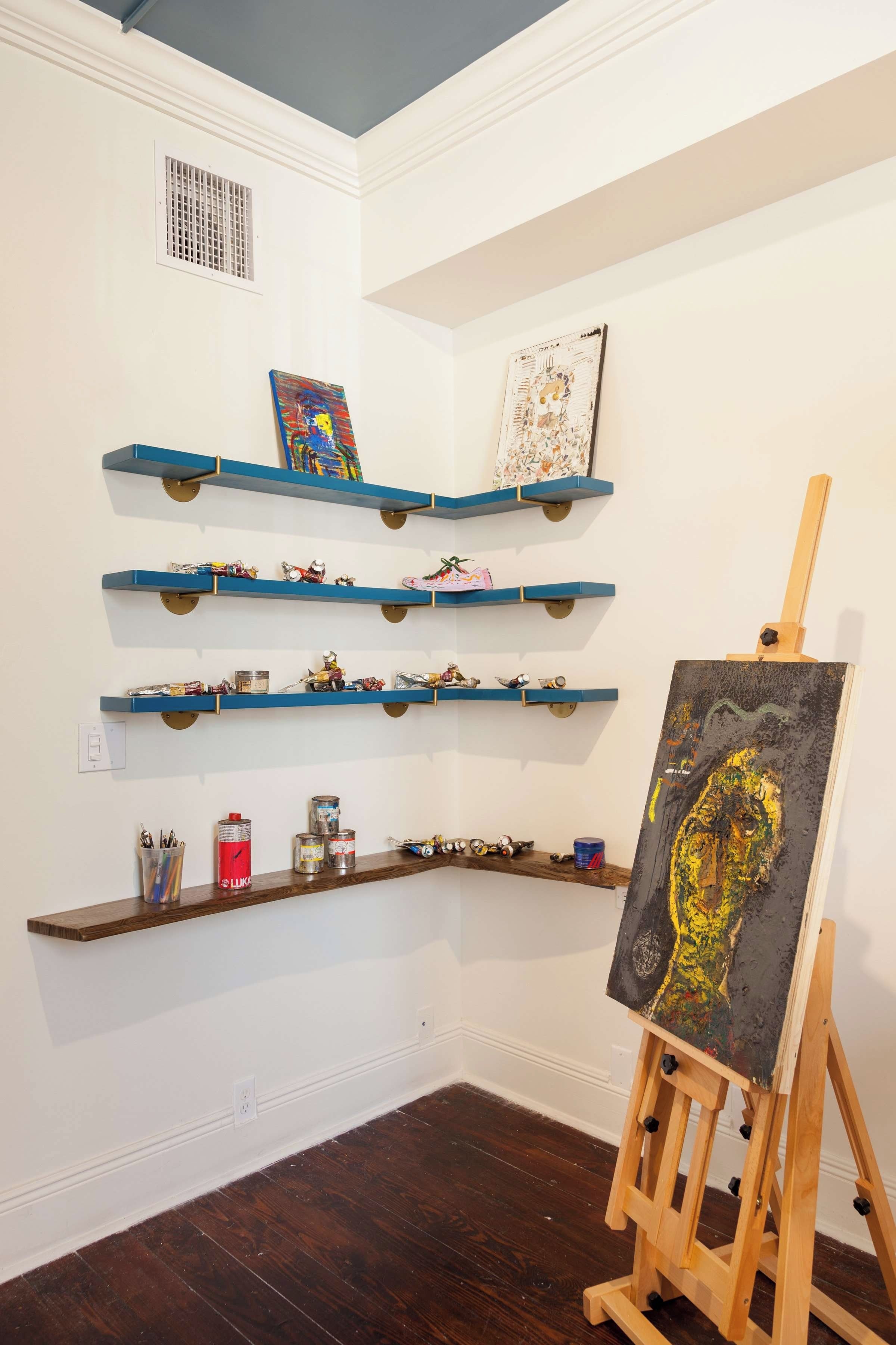 Una habitación con paredes blancas, suelo de madera oscura y varios estantes azules con diversos objetos.