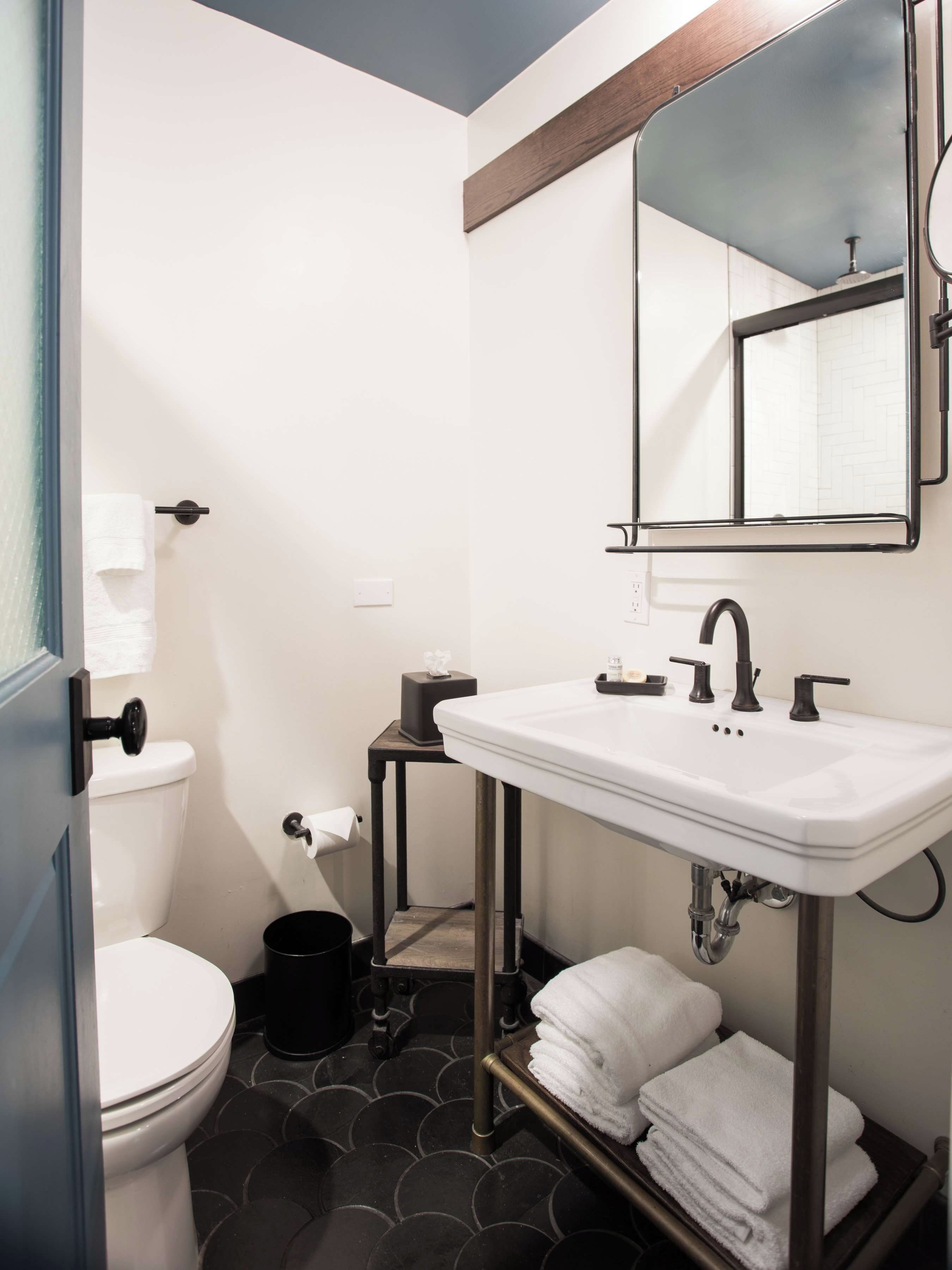 A bathroom with a white sink, black fixtures, a mirror, and a toilet.