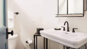 Ein Badezimmer mit einem weißen Waschbecken, schwarzen Armaturen, einem Spiegel und einer Toilette.