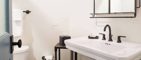 A bathroom with a white sink, black fixtures, a mirror, and a toilet.