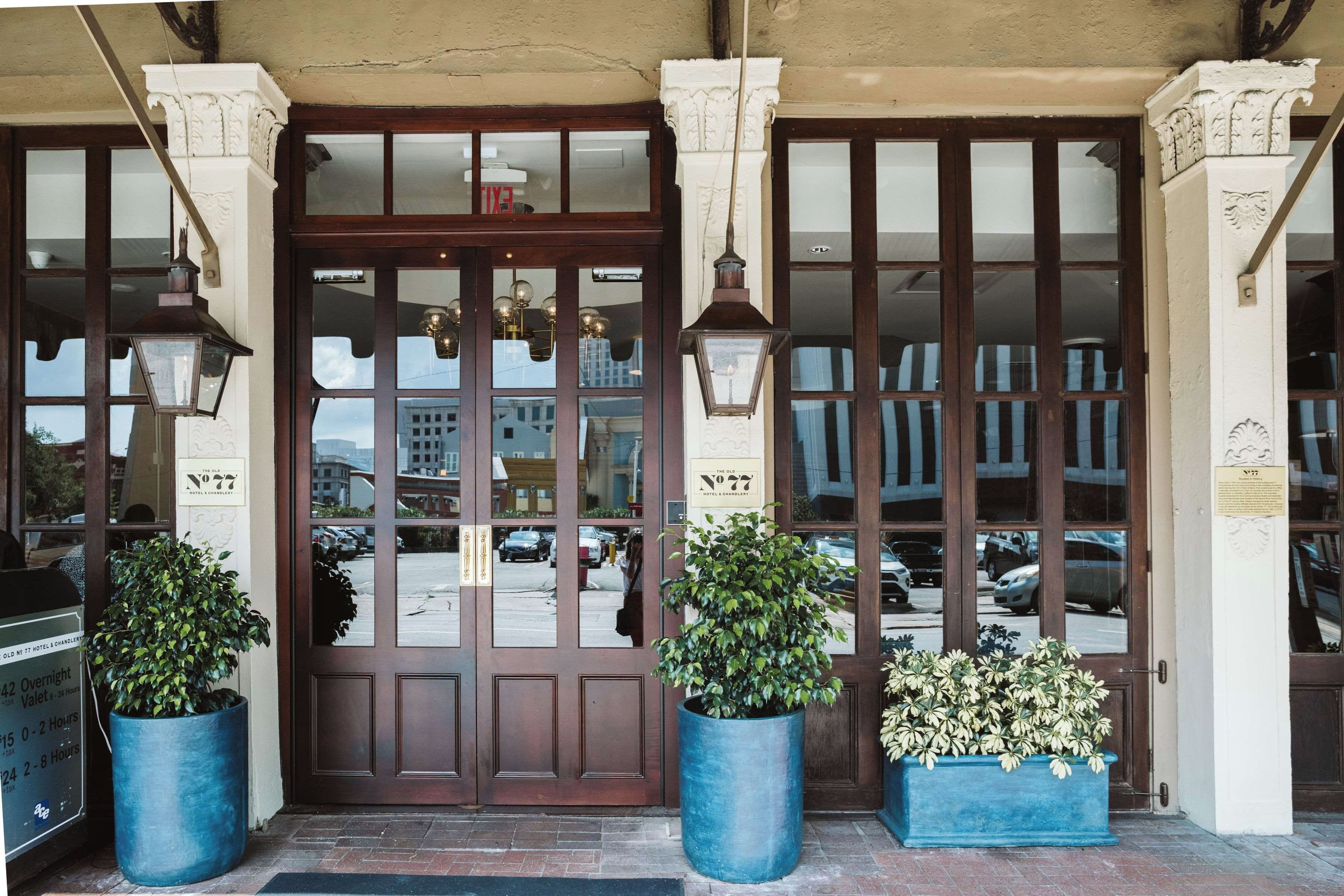 A hotel entrance with a large wooden double door, two large potted plants, and a sign indicating the hotel name.