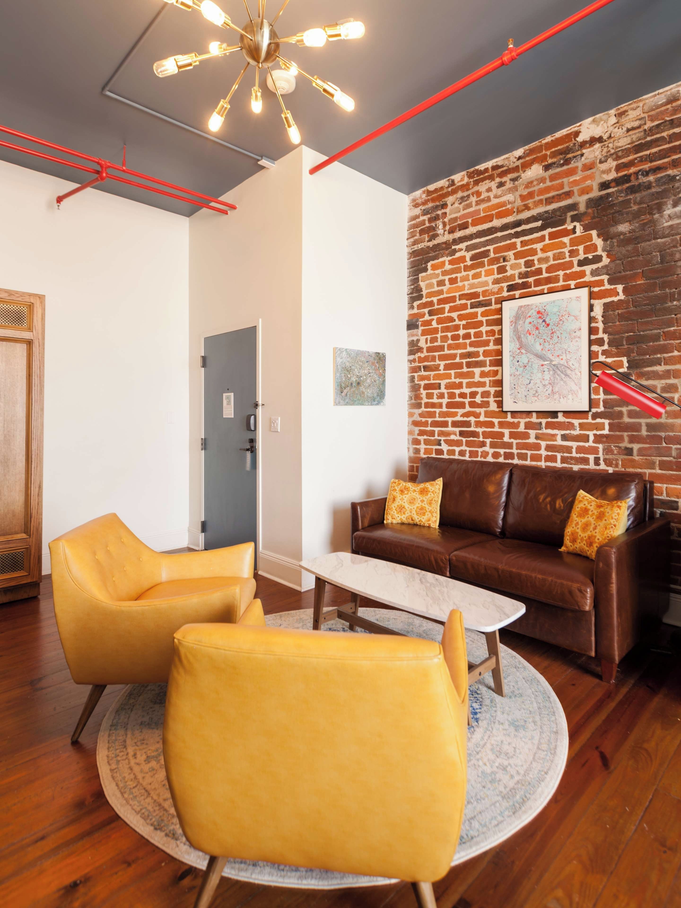A modern living room with a brick wall, leather sofa, yellow armchairs, and a round coffee table.