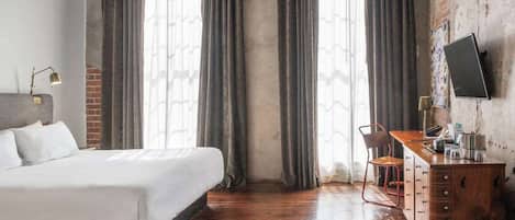 A hotel room with a bed, a desk with a chair, a TV, and a dresser.