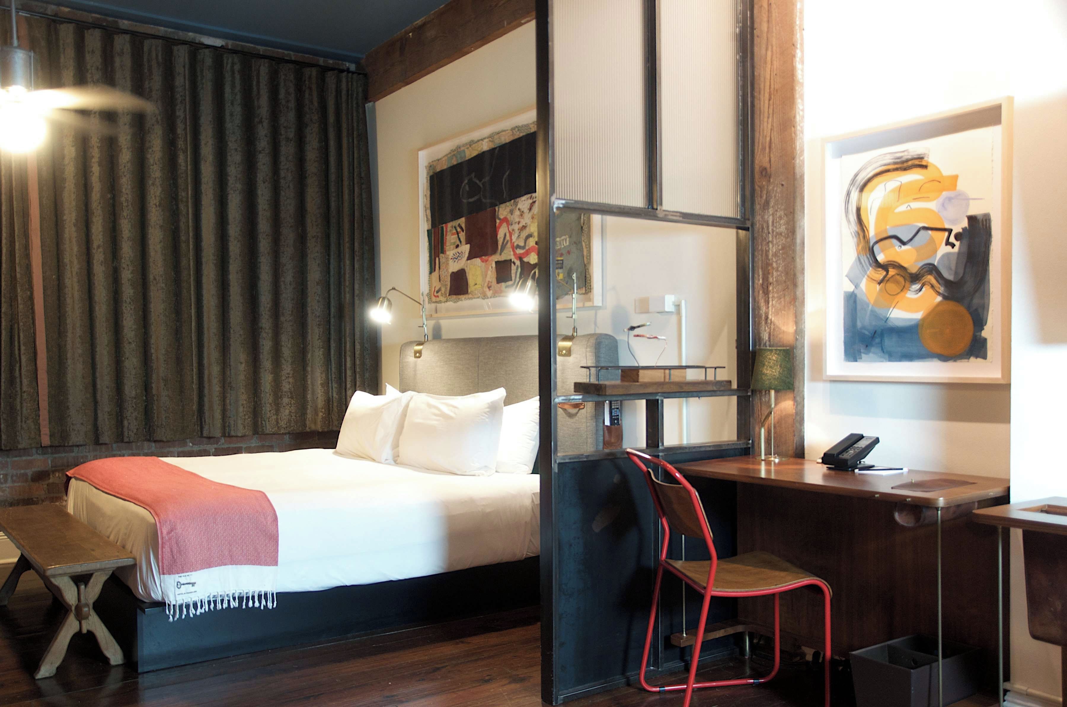 Een hotelkamer met een bed, een bureau, een stoel, een lamp en kunst aan de wanden.