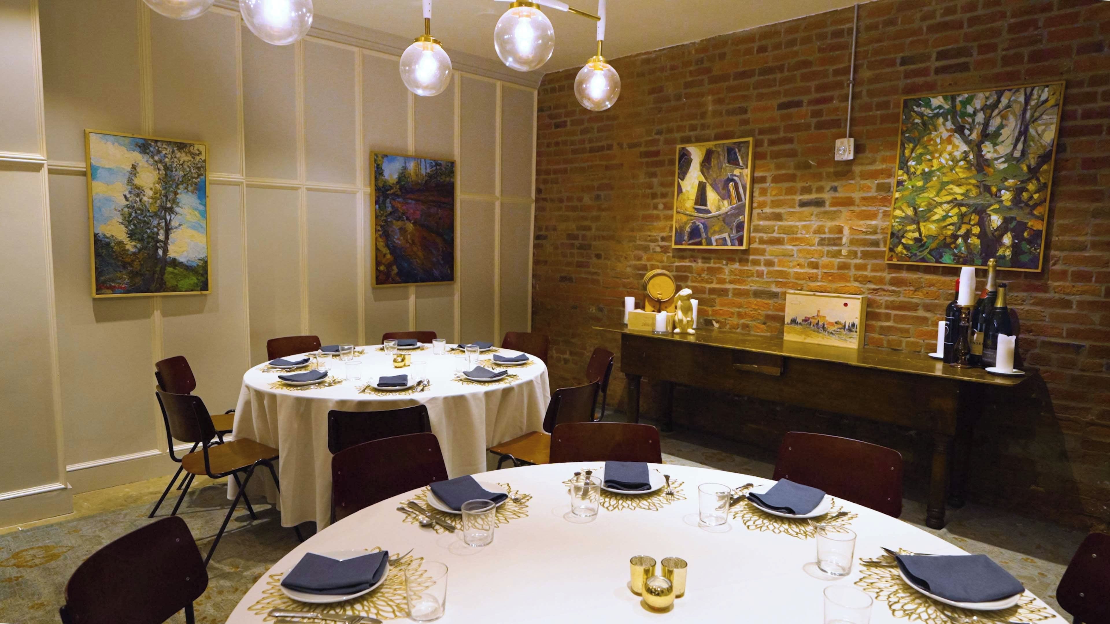 A dining area with round tables set for four, each with white tablecloths, gold leaf accents, and dark blue napkins.