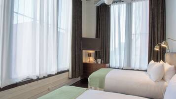 A hotel room with two beds, a flat-screen TV, a desk with a lamp, and a ceiling fan.