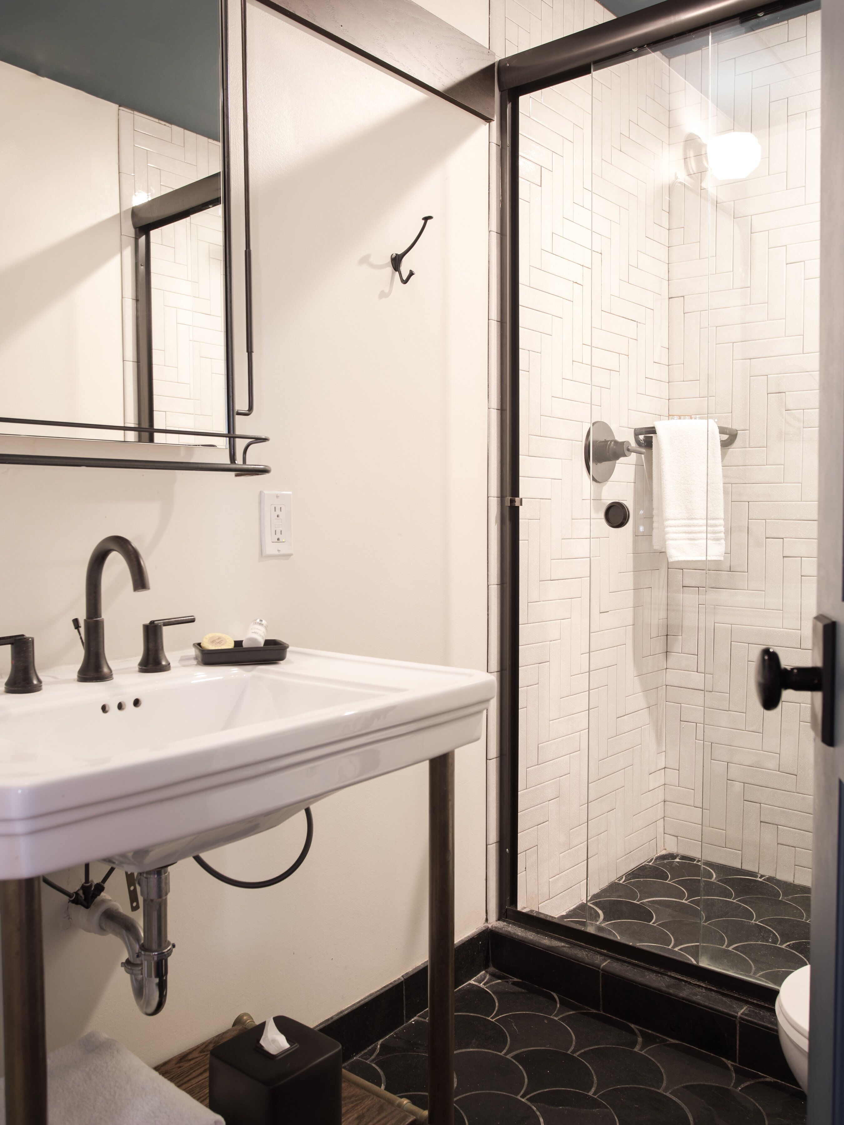 A bathroom with a white sink, black faucets, and a glass shower enclosure with a black and white tiled floor.