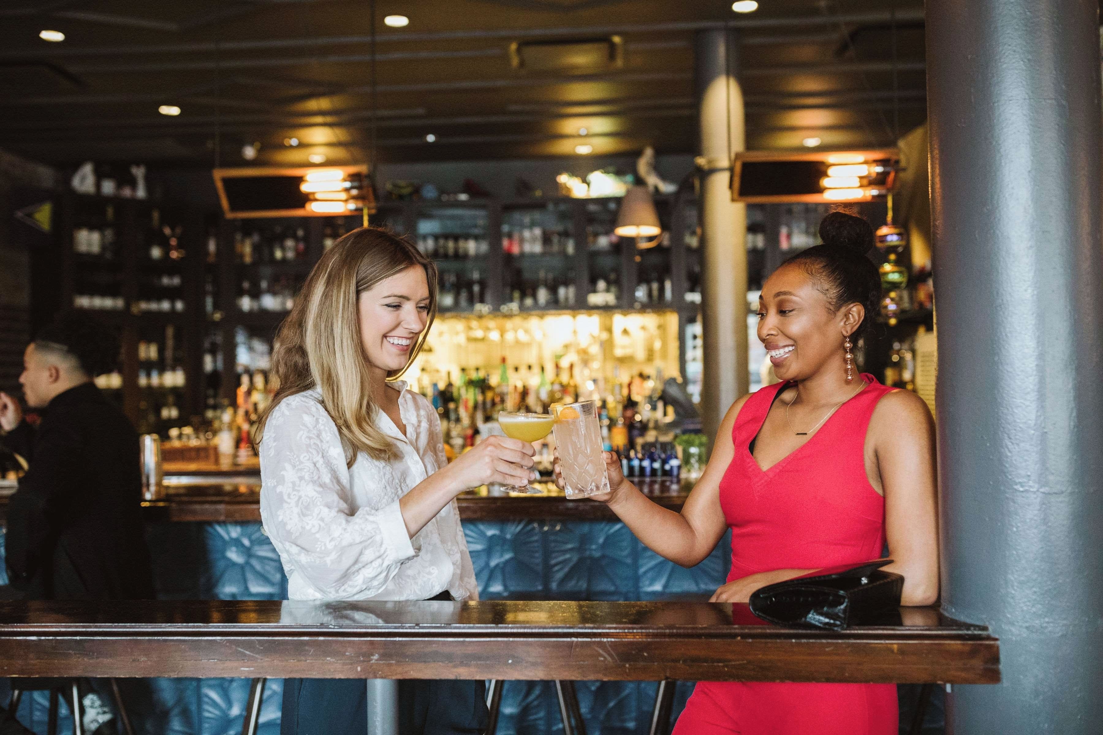 Two individuals at a bar with a variety of bottles in the background.