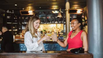 Two individuals at a bar with a variety of bottles in the background.