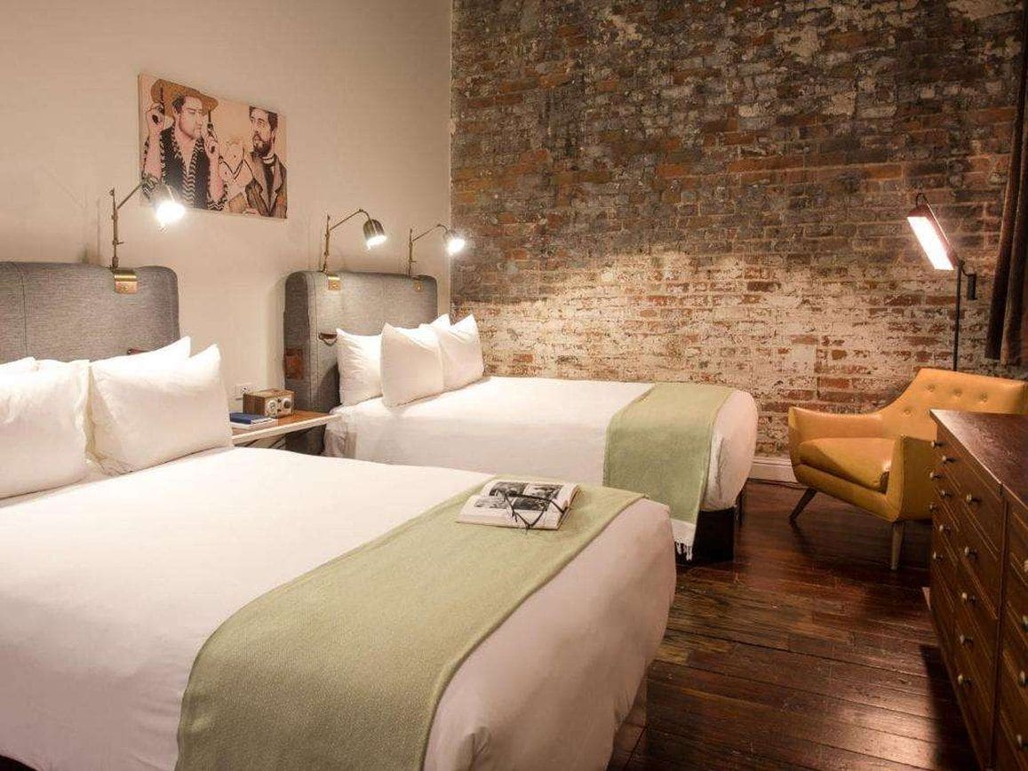 Ein Hotelzimmer mit zwei Betten, einer Ziegelwand, einem Holzboden und einem gelben Sessel.