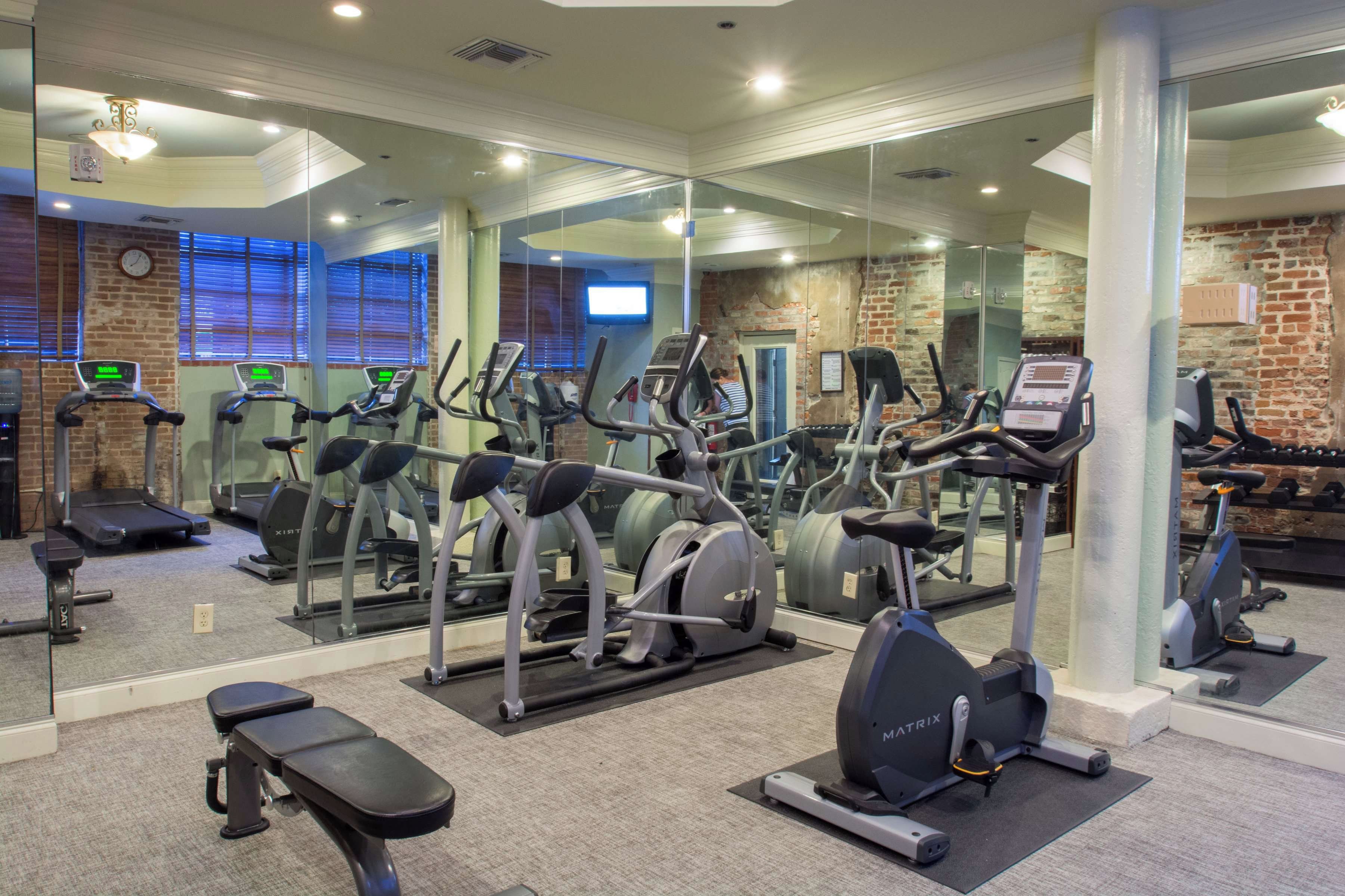 Une salle de sport équipée de divers appareils de cardio, d’un banc et d’un mur recouvert de miroirs.