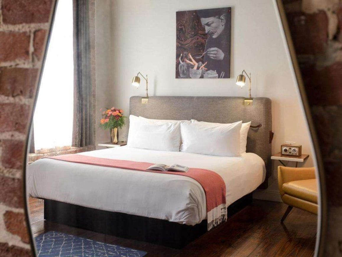 A bedroom with a bed, bedside lamps, a nightstand, a chair, and a painting on the wall.