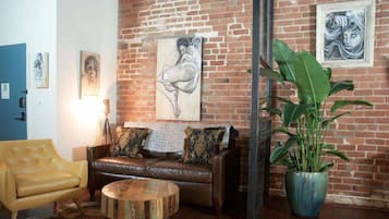 A room with a brick wall, a leather sofa, a round coffee table, and a large potted plant.