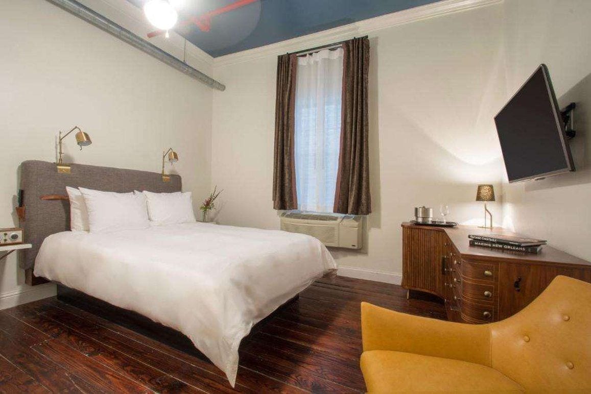 Ein Hotelzimmer mit Bett, Schreibtisch, Stuhl, Fernseher und einem Fenster mit Vorhängen.