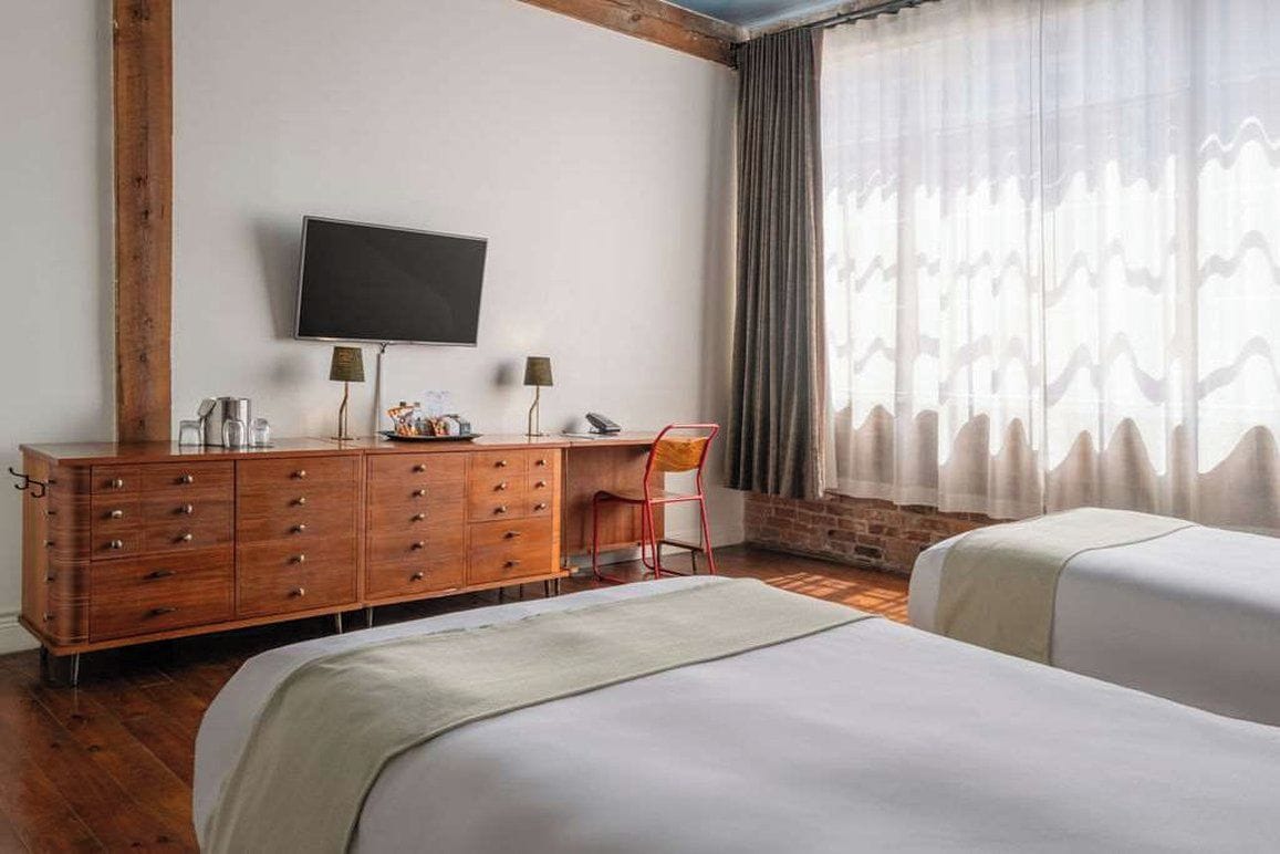 Habitación de hotel con cómoda de madera, televisor montado en la pared, escritorio con lámpara, una silla y dos camas.