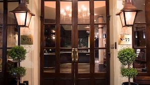 A hotel entrance with a dark wooden double door, two potted plants, and two wall-mounted lanterns.