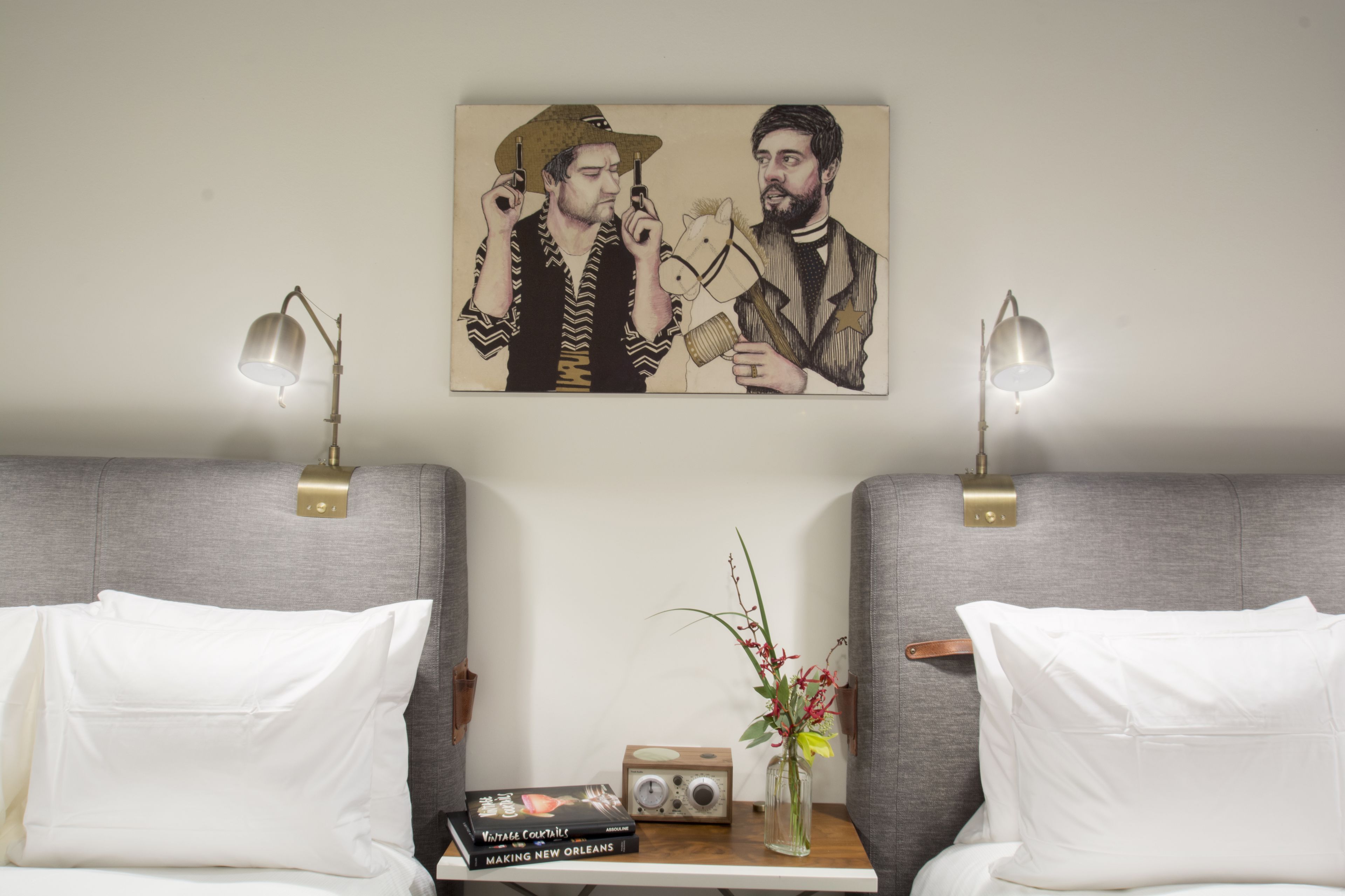 A hotel room with two beds, a bedside table with a radio and a book, and a painting on the wall.