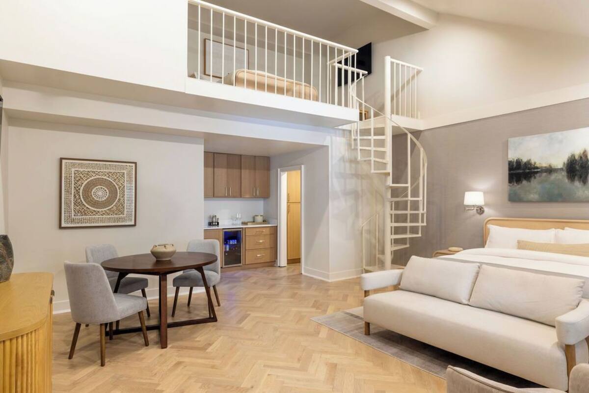 Ein geräumiger Wohnbereich mit hoher Decke, einem Esstisch, einer Couch und einer Treppe, die in ein Obergeschoss führt.