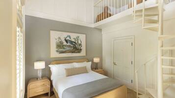 A bedroom with a bed, bedside tables, a nightstand, a framed picture on the wall, a door, and a staircase.