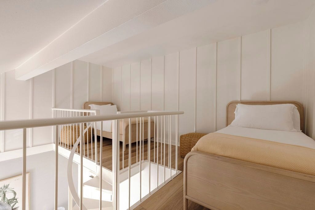 A bedroom with a wooden bed, a white railing, and a view of the outside.