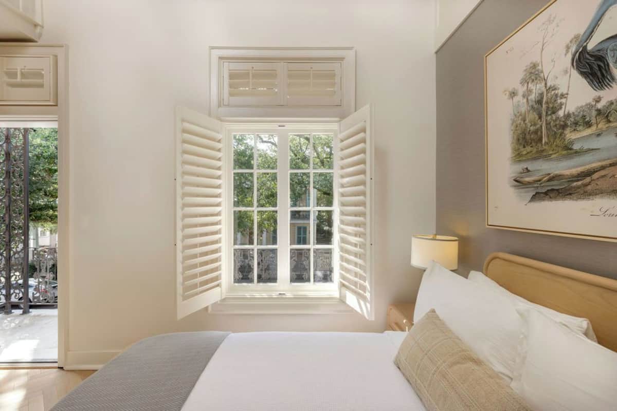 Ein Schlafzimmer mit einem großen Bett, einem Fenster mit Rollläden, einer Wandlampe und einem gerahmten Bild.