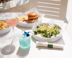 Ein Tisch mit Salat, Burger, Pommes und einem rosafarbenen Getränk.