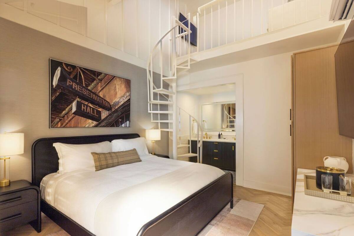 Ein Schlafzimmer mit einem großen Bett, einer weißen Wendeltreppe, einem Spiegel und einer kleinen Küchenzeile.