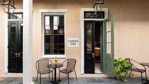 Ulkona on istuinalue, jossa on pöytä ja tuoleja, ja siinä on kyltti, jossa lukee ”GARDEN BAR”, sekä ovi, joka johtaa baarialueelle.