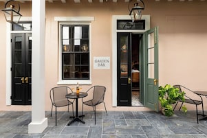 Un espace extérieur aménagé avec une table et des chaises, une enseigne indiquant « BAR DE JARDIN », et une porte donnant accès à l’intérieur du bar.