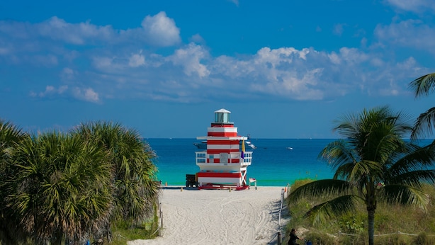Una spiaggia con un faro rosso e bianco, cielo azzurro limpido e mare color turchese.