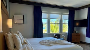 Camera d'hotel con un ampio letto, una scrivania, una sedia, una televisione e una finestra con tende.