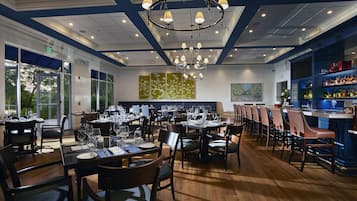 Een restaurant met meerdere eettafels, stoelen, een bar en een grote kroonluchter.
