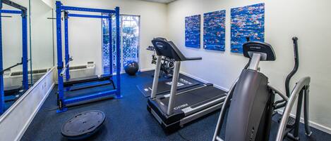 A gym with exercise equipment, including a treadmill, elliptical, and weightlifting station.