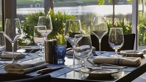 A dining table set with wine glasses, plates, and cutlery, with a view of a lake and greenery through a window.