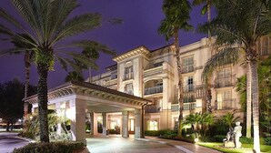 A multi-story hotel with a covered entrance, palm trees, and a well-lit facade.