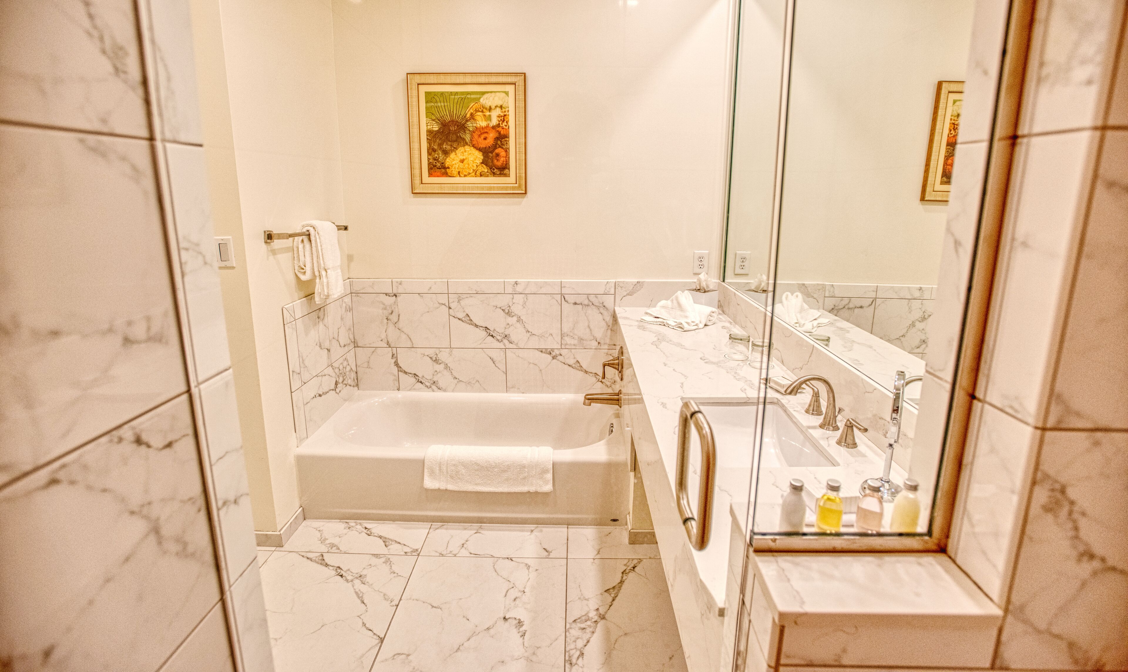 Un bany amb sòl de marbre, una banyera, un lavabo amb mirall i una fotografia encadrada a la paret.