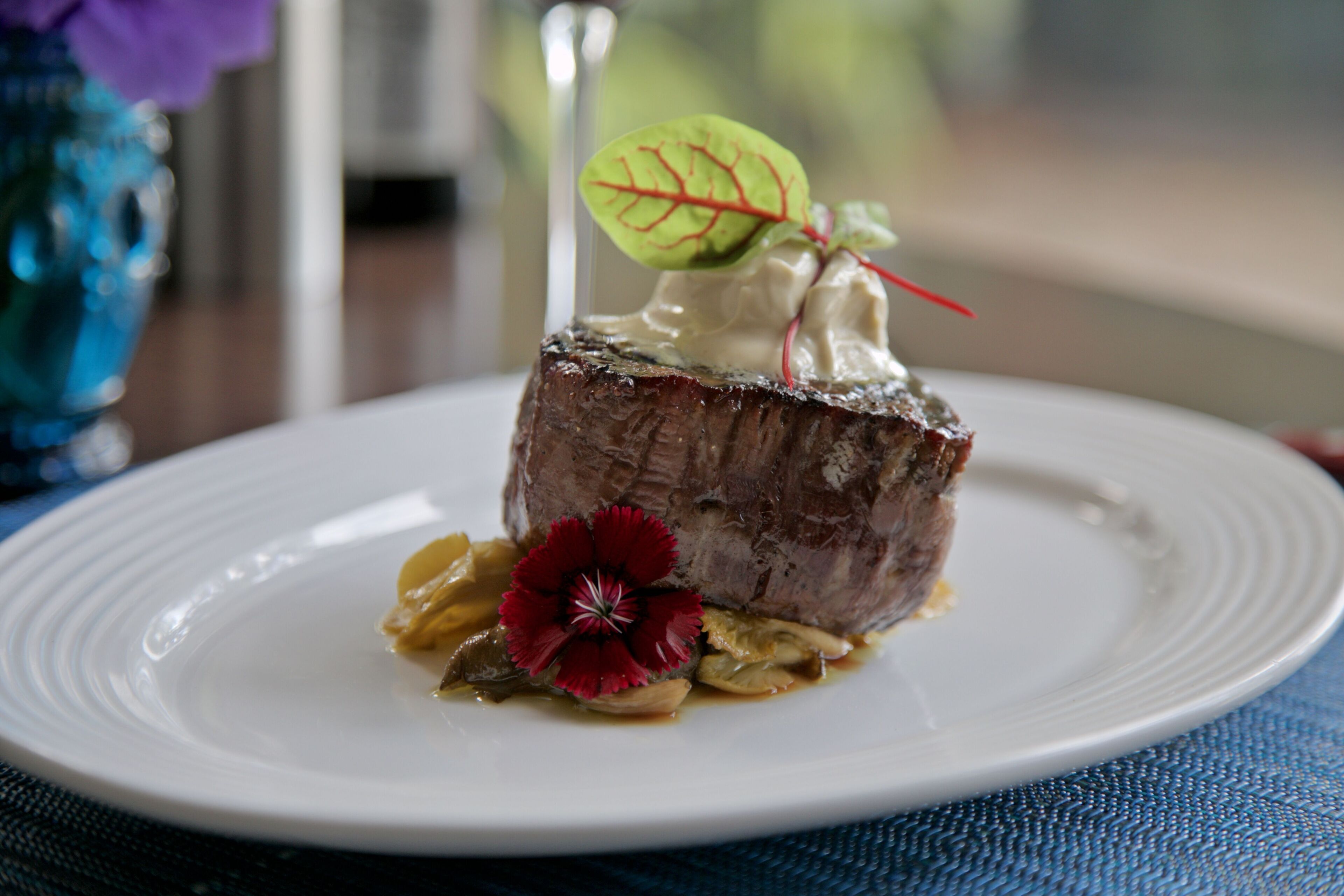 Ein Teller mit Fleisch, einer roten Blume und einem grünen Blatt als Garnitur.